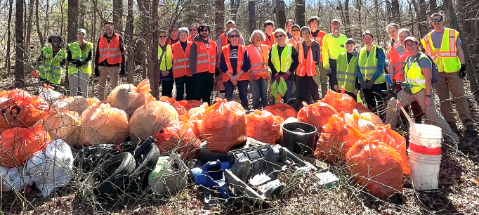 A group of volunteers stands behind more than 20 bags of trash that was collected at the mouth of Ellerbe Creek.