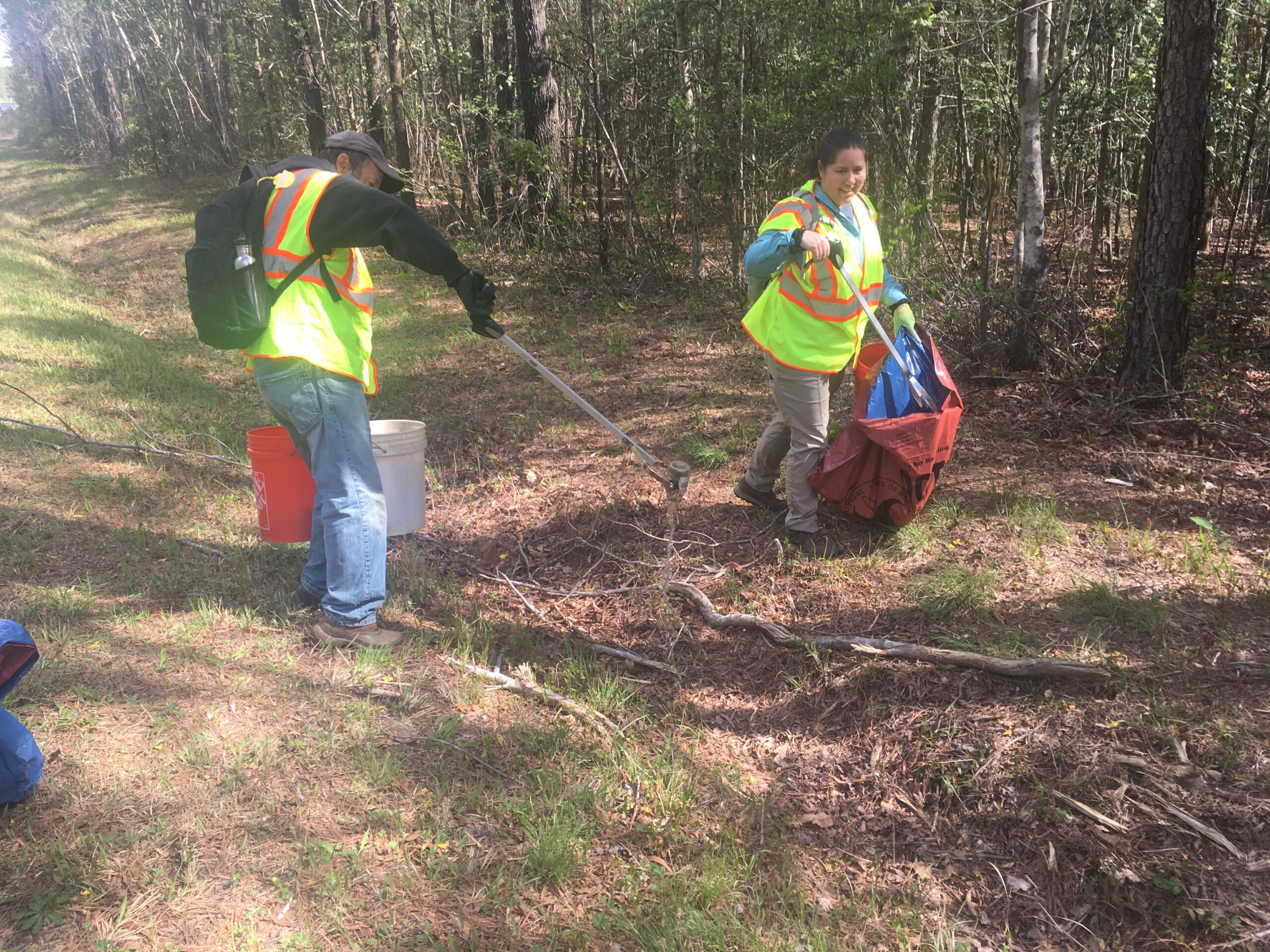 Two volunteers use pickers to clean up trash near the Upper Little River.