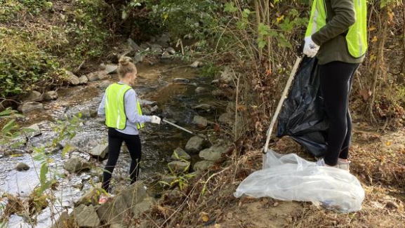 A volunteer using a trash picker to clean up trash in Rocky Branch Creek.