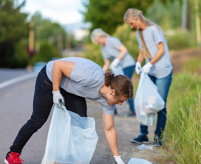 Three college students picking up trash along the side of a road.