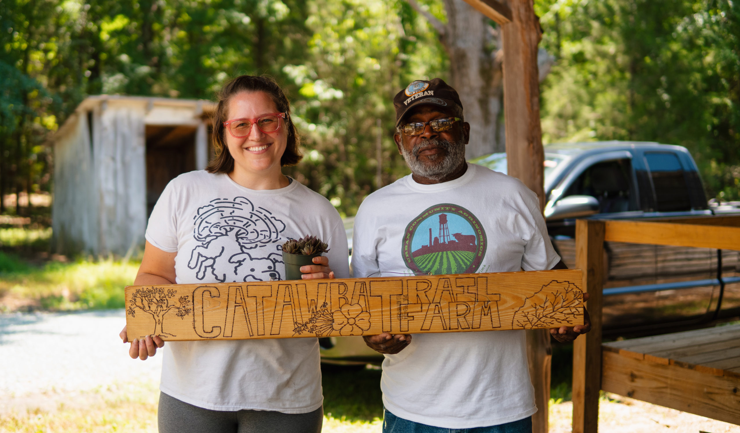 Two people holding a wooden sign that says Catawba Trail Farm.