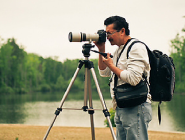 Wildlife Photographer looking through a telephoto lens in front of a pond