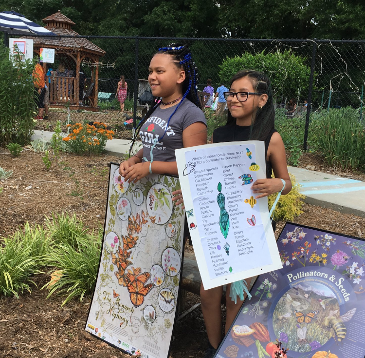 Two young girls holding signs about pollinators at the Winterfield Community Garden.