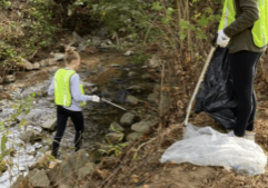 A volunteer using a trash picker to clean up trash in Rocky Branch Creek.