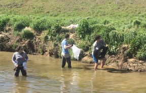 Three people in waders pulling trash from a creek and bringing it to the shore.